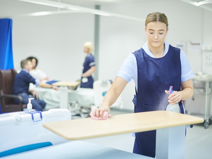 A woman cleans a tabletop in the common area of a health care environment