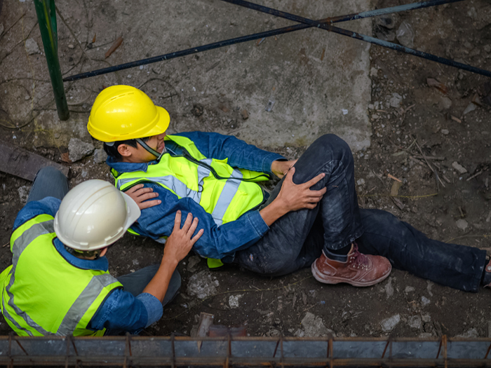 An injured worker grabbing his leg is attended to by a coworker