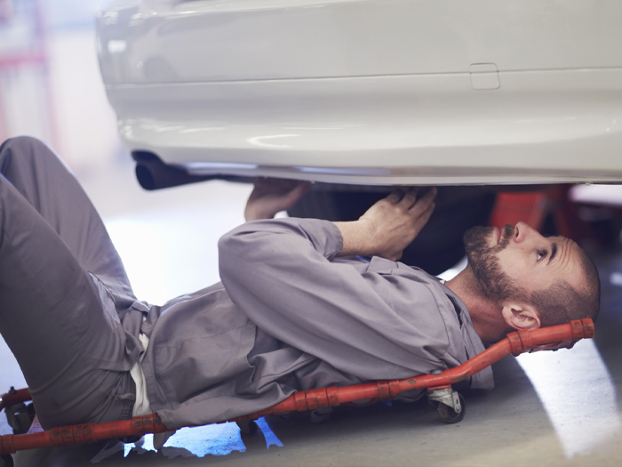 A man on a mechanic's dolly inspects the undercarriage of an automobile