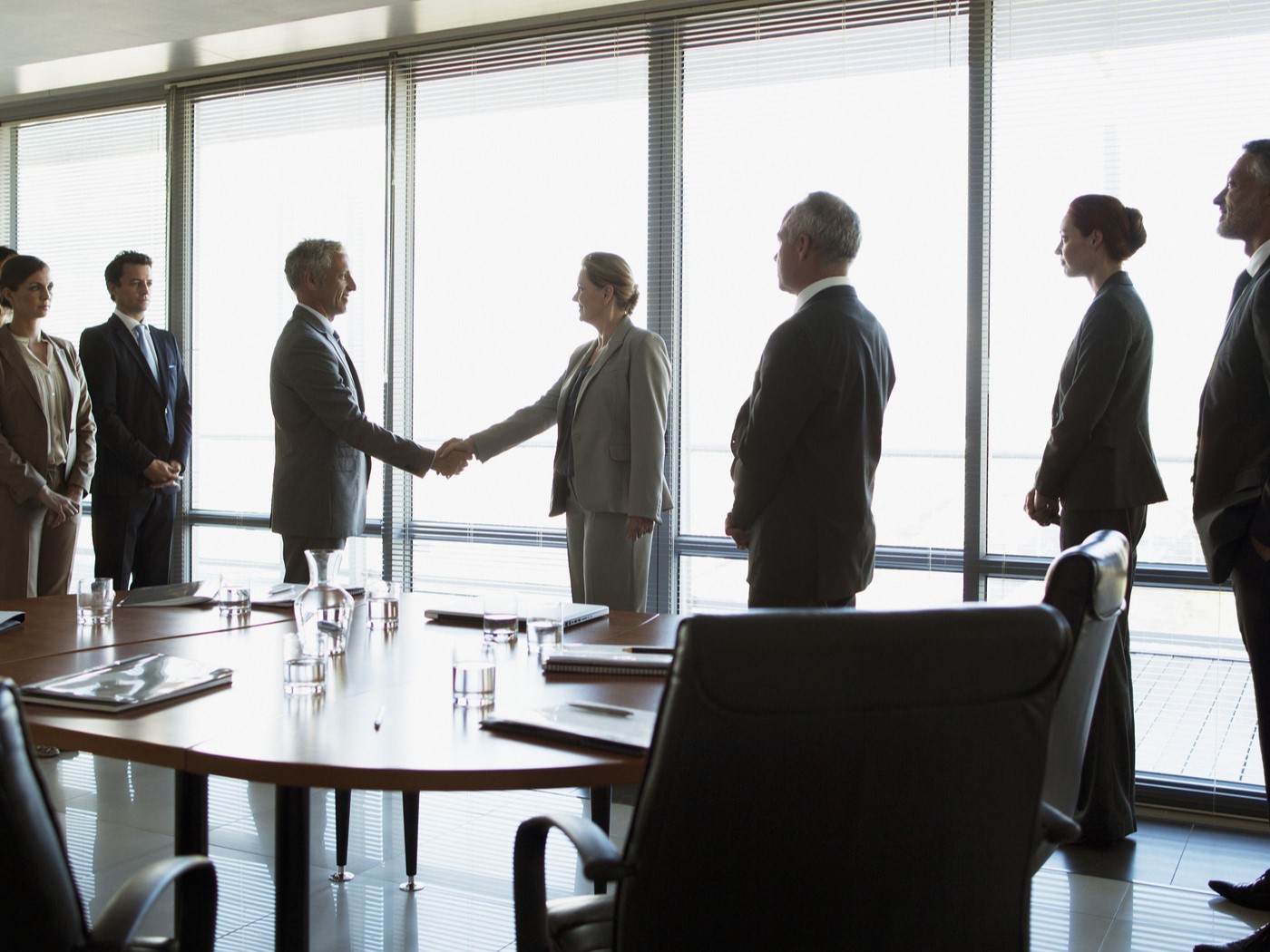 Two people shaking hands in conference room as other executives look on