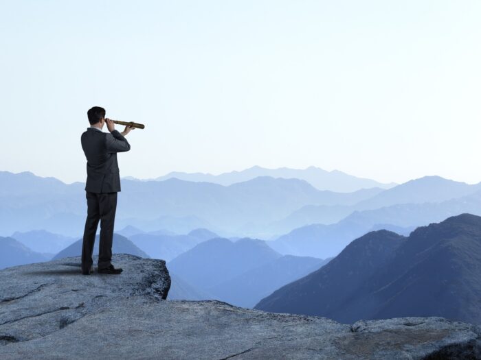 Businessman With Spyglass Looking Out Toward Mountain Range