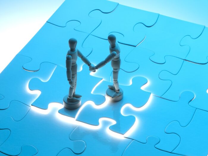 Business agreement concept with wooden figures shaking hands on a jigsaw puzzle