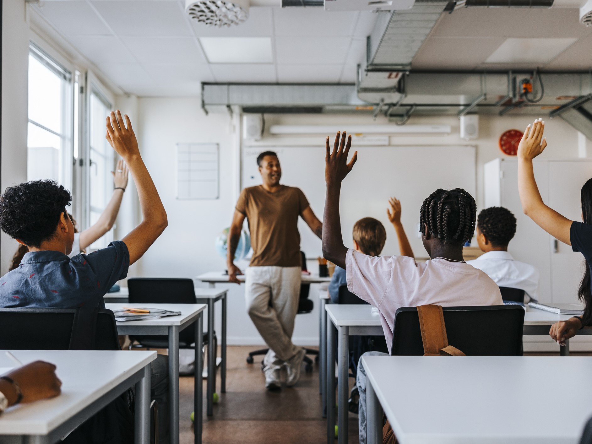 junior high students with hand raised while teacher teaching in classroom at school