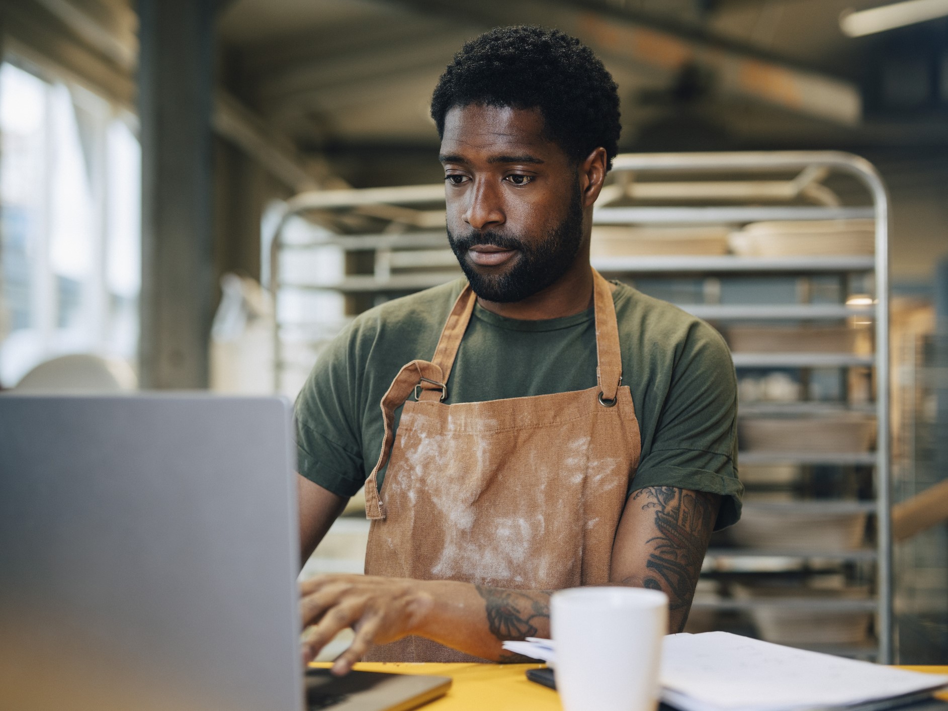Male baker wearing apron and working on laptop at baker