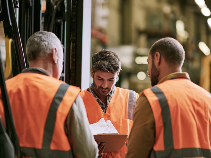 warehouse workers in safety vests review a clipboard.